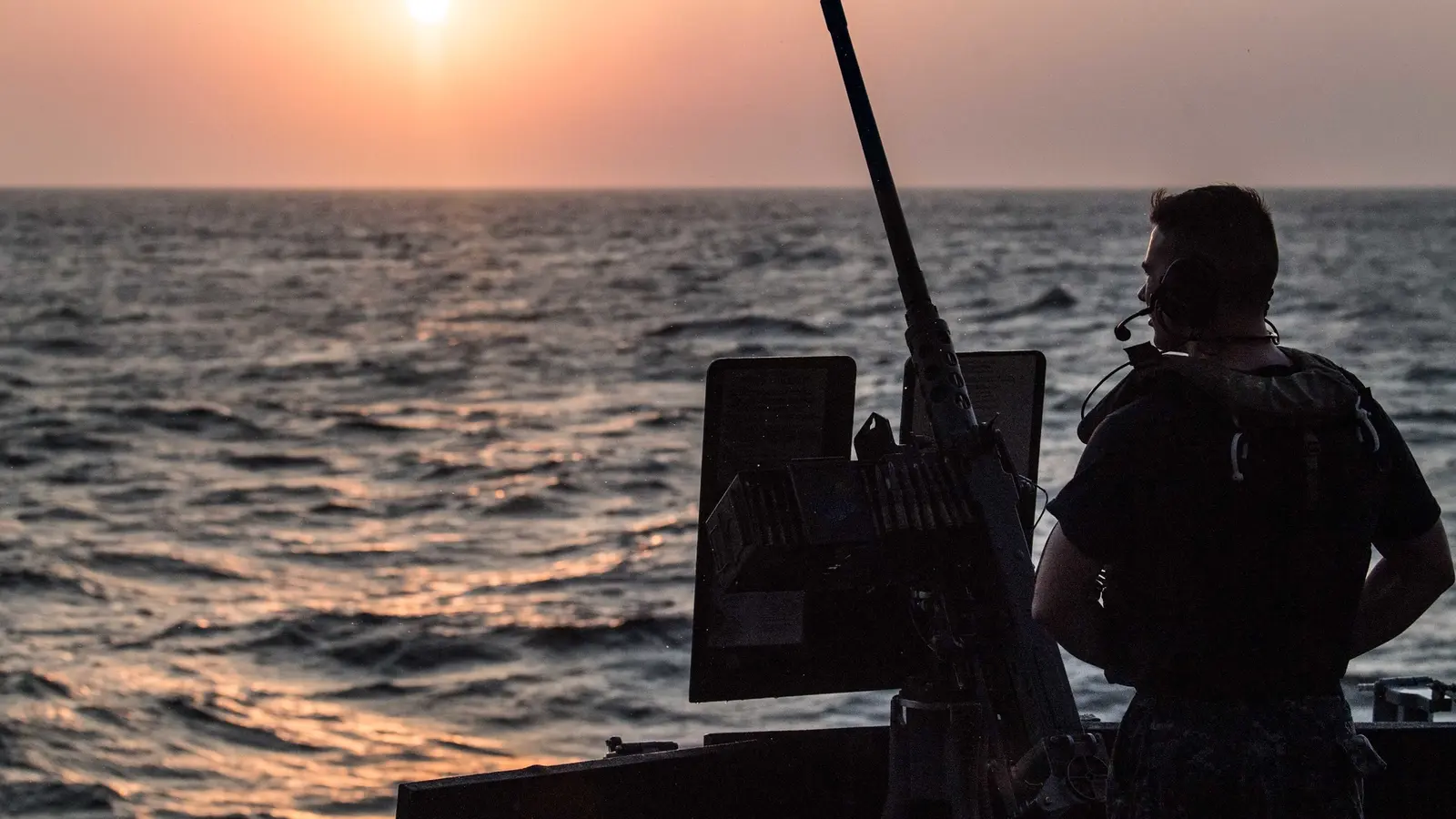 A U.S. Navy sailor stands watch aboard USS Jason Dunham while transiting the Bab al-Mandeb Strait at sunset