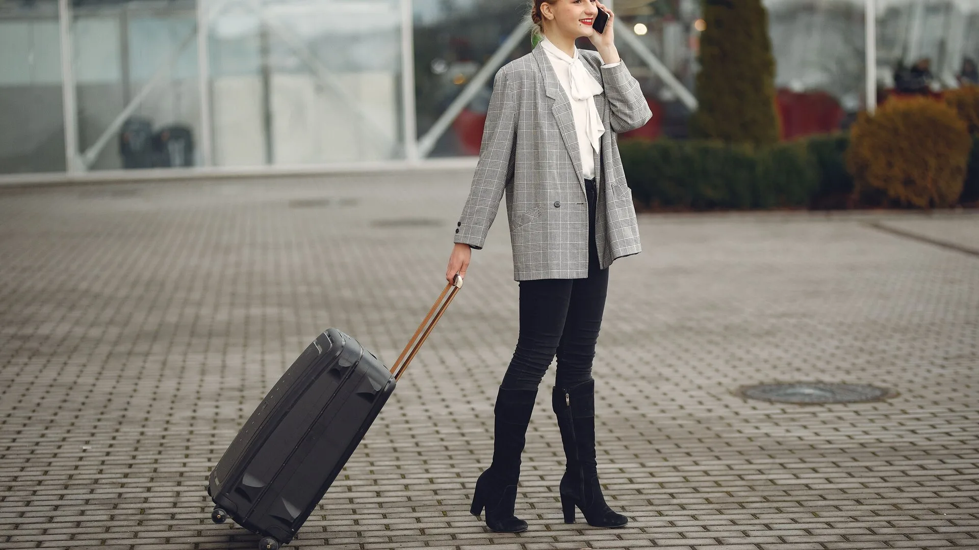 Traveler using a smartphone while pulling luggage outside an airport